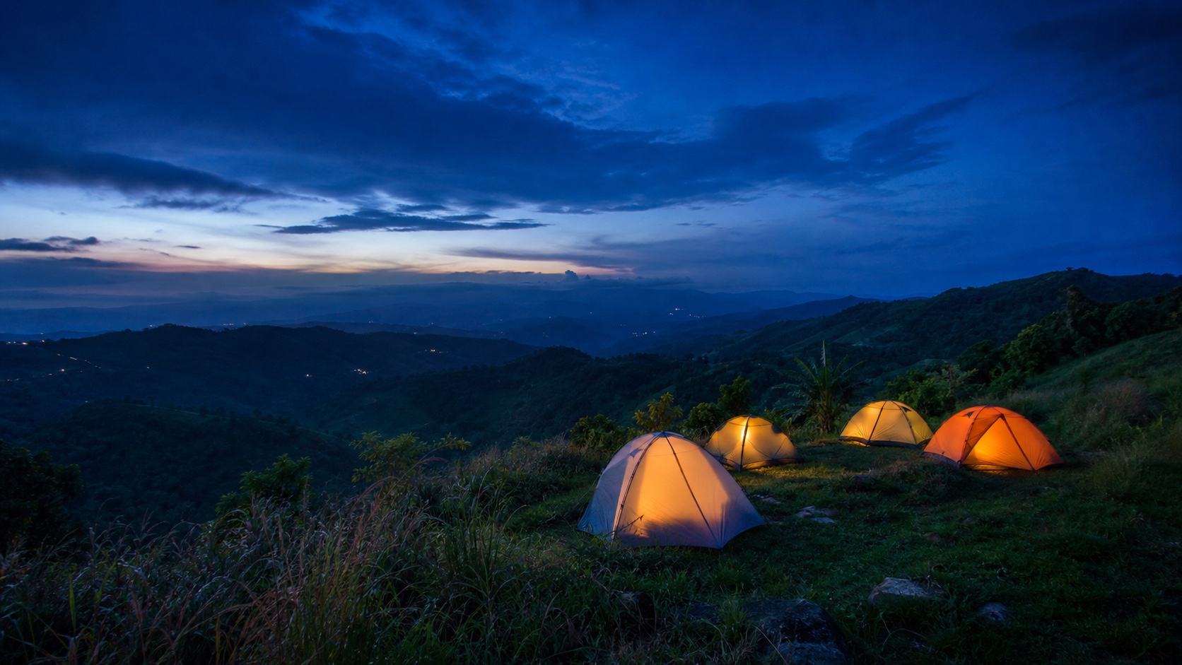 Warmly lit tents overlooking layered Cebu-inspired highland ridges at blue hour